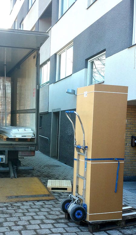 Kolimisteenus Tartus – suur kast rihmaga kinnitatud kärule, kolimisauto tagaluuktõstuki juures kortermaja ees.