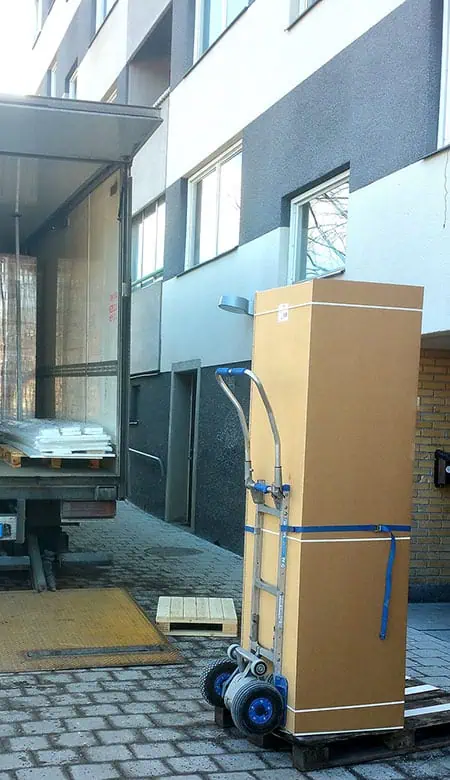 Kolimisteenus Tartus – suur kast rihmaga kinnitatud kärule, kolimisauto tagaluuktõstuki juures kortermaja ees.